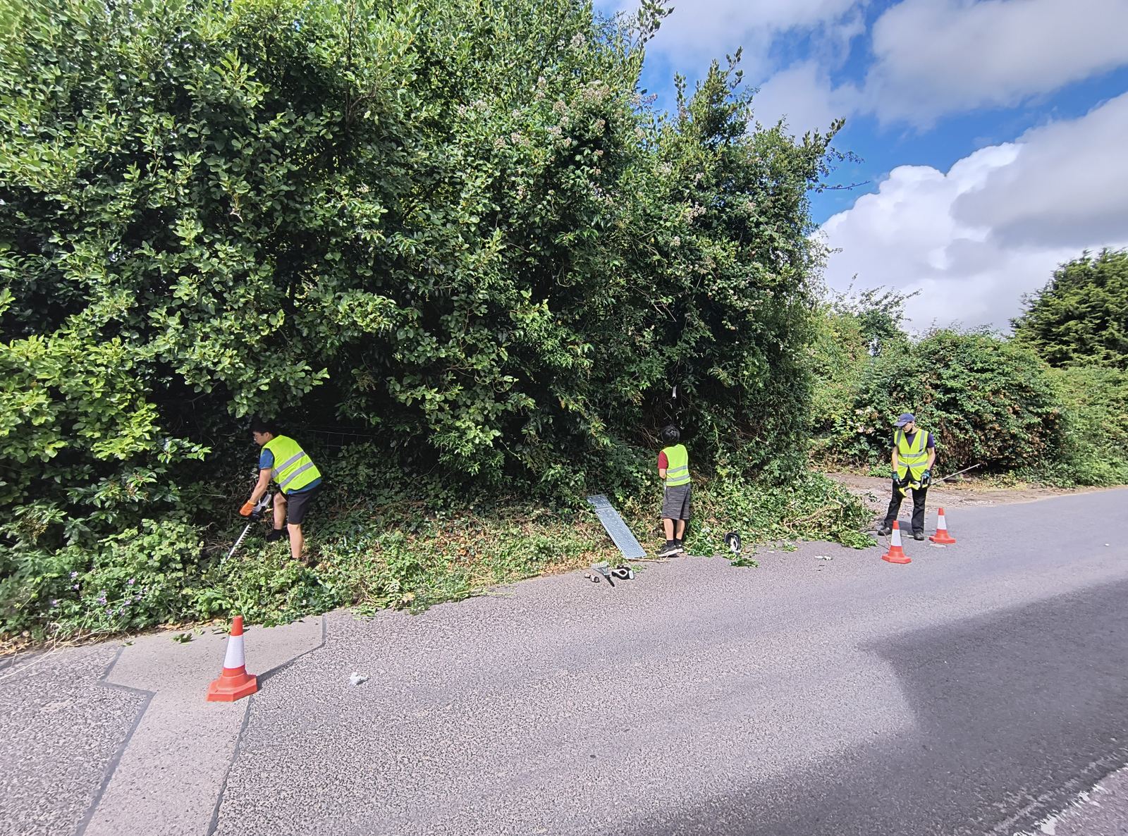 Crew in high-visibility clothing cutting the tall Woodnesborough hedge back from behind traffic cones